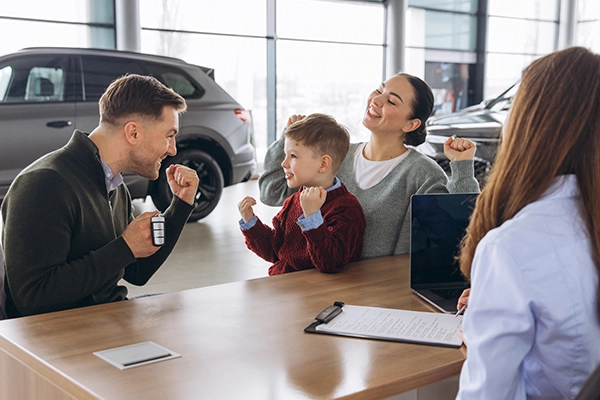 Family celebrating successful car purchase at modern dealership, receiving new car keys